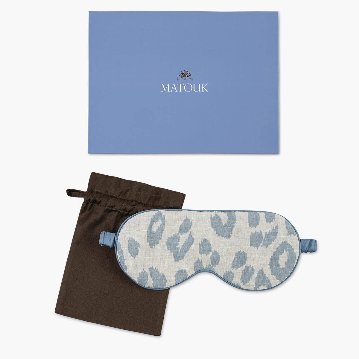 Sleep mask with blue leopard print, black drawstring bag, and blue Matouk branded box on a white background