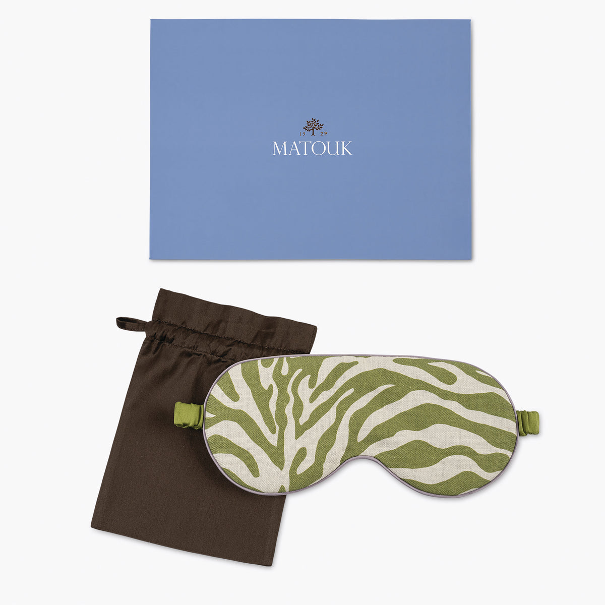 A green and white zebra print Matouk sleep mask with a brown pouch, shown in front of a blue Matouk branded box.