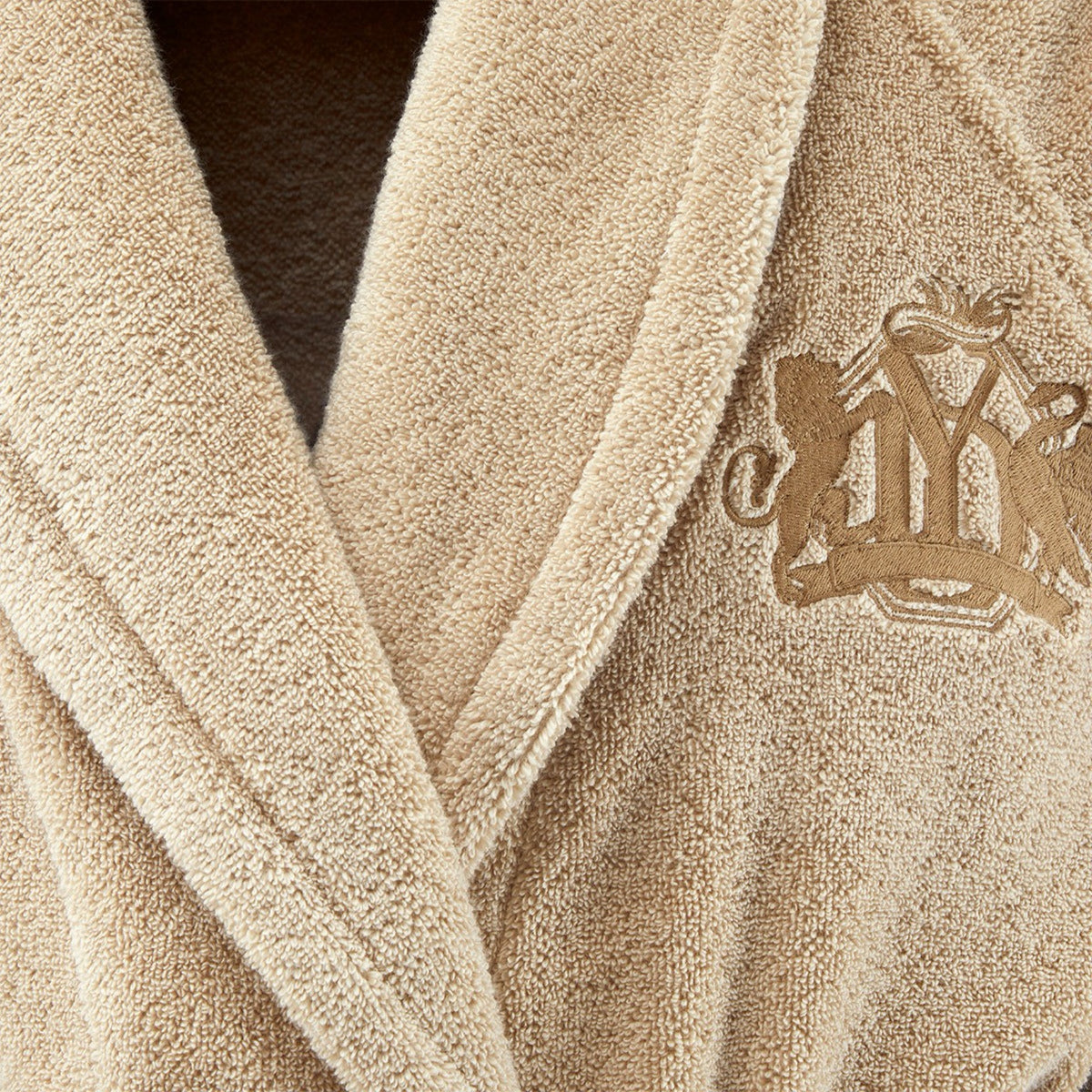 Close-up of Yves Delorme Apollon Bath Robe in Dune color with an embroidered crest, crafted from organic cotton bath towels.