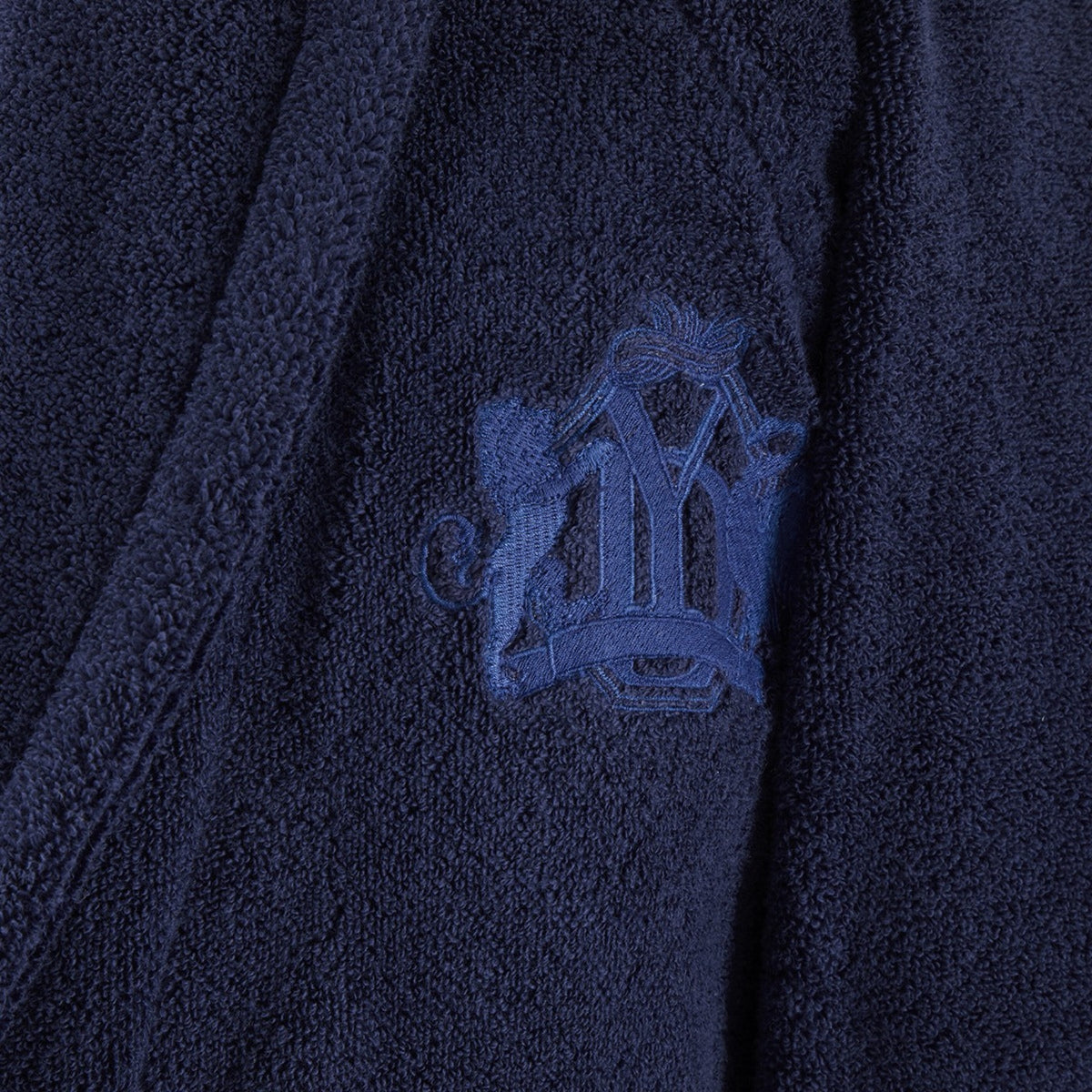 Close-up of Yves Delorme Apollon Bath Robe in Marine color with an embroidered crest, crafted from organic cotton bath towels