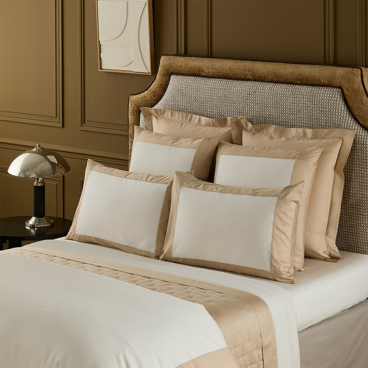 Closeup of Yves Delorme Apollon Dune Bedding Collection, set against a brown wall and bedframe