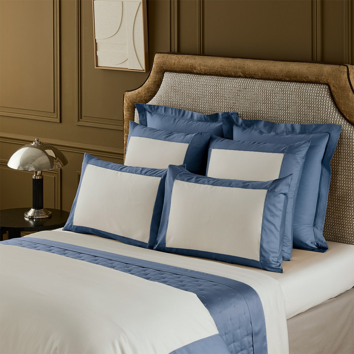 Closeup of Yves Delorme Apollon Outremer Bedding Collection, set against a brown wall and bedframe