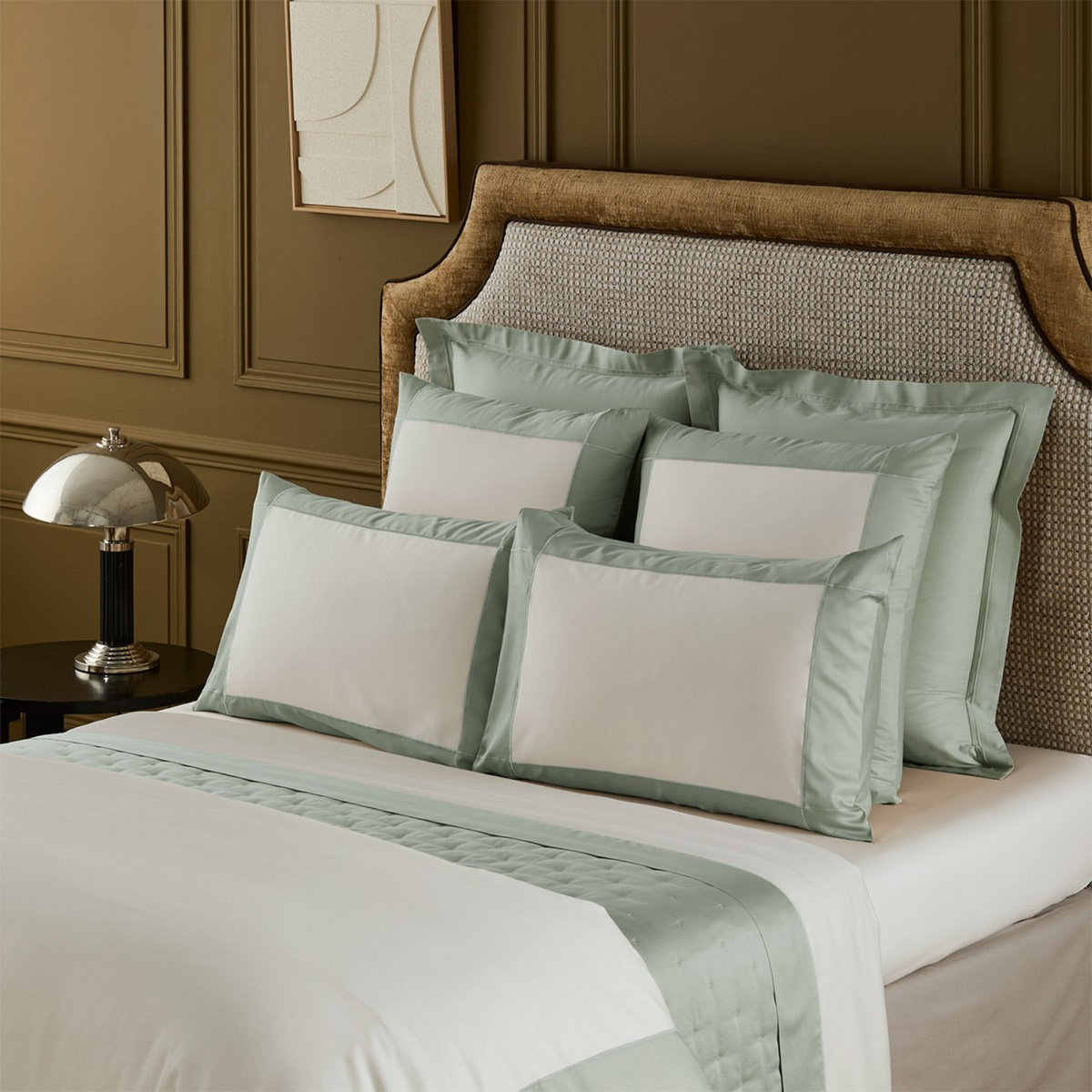 Closeup of Yves Delorme Apollon Veronese Bedding Collection, set against a brown wall and bedframe