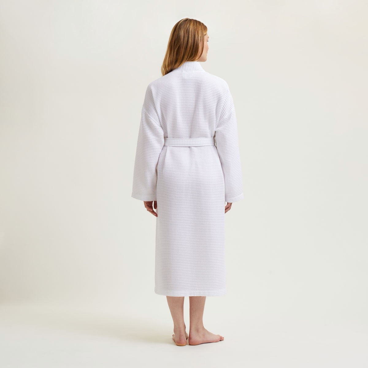 A woman stands barefoot facing away, wearing Pierre Yves Delorme Astreena Bath Robe, against a plain light background
