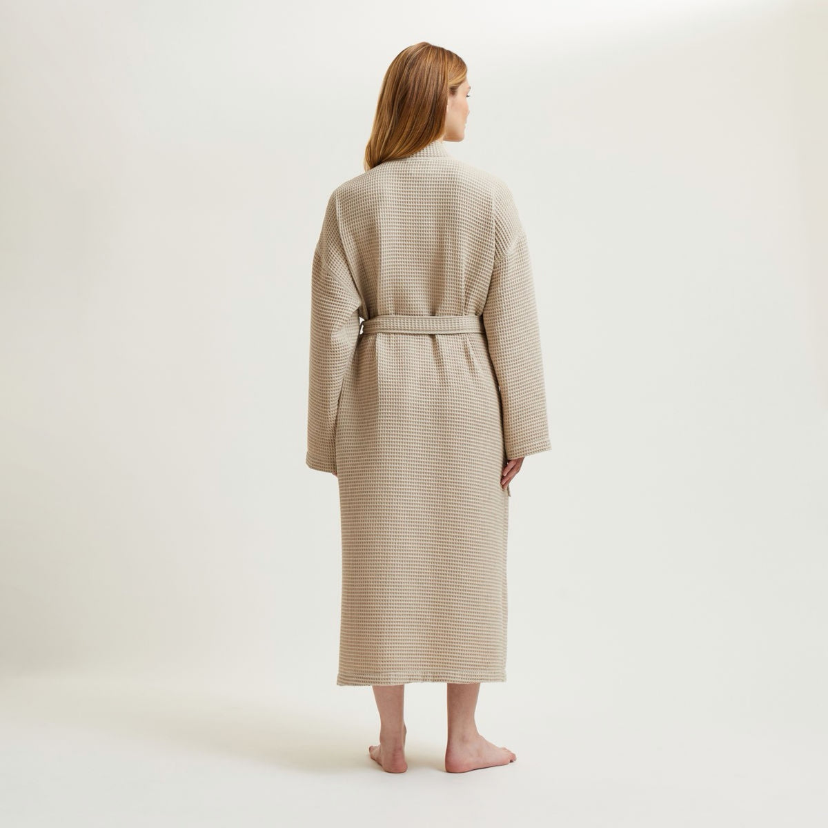 Woman in a Pierre Yves Delorme Astreena Bath Robe stands barefoot, facing away, against a plain background