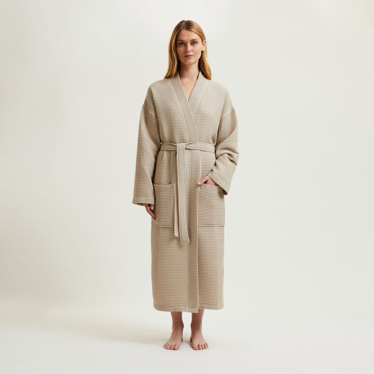 Woman stands barefoot in a Pierre Yves Delorme Astreena Bath Robe, against a plain light background.