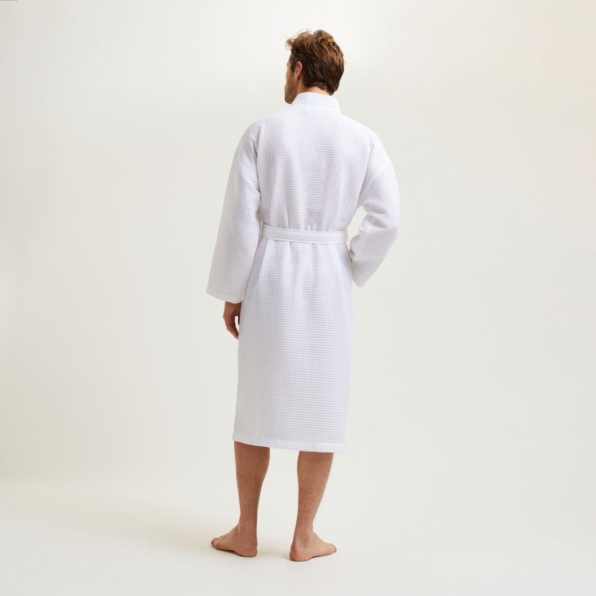 A man stands barefoot facing away, wearing a Blanc Yves Delorme Astreena Bath Robe, against a plain white background