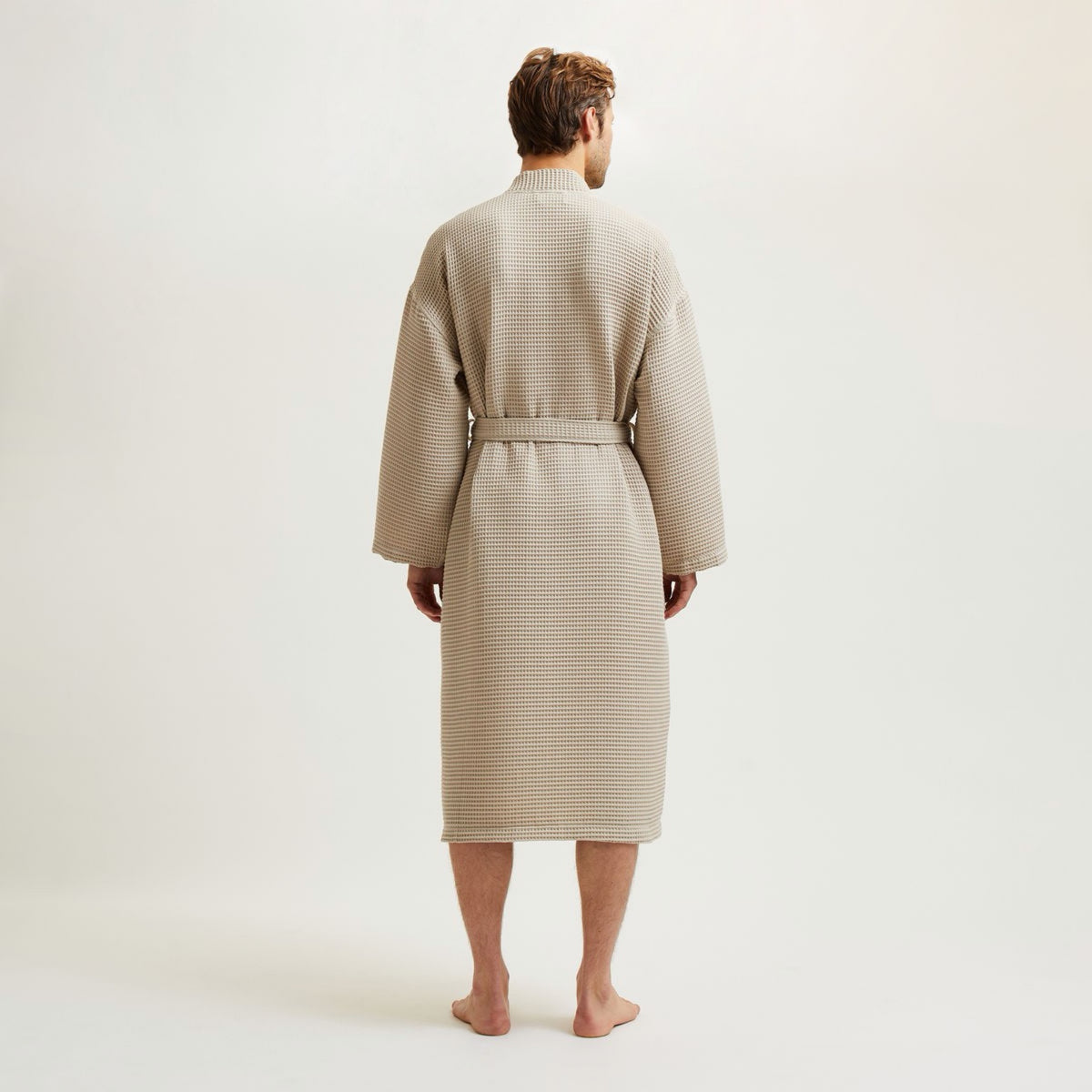 A person stands barefoot, wearing a Pierre Yves Delorme Astreena Bath Robe, against a plain background