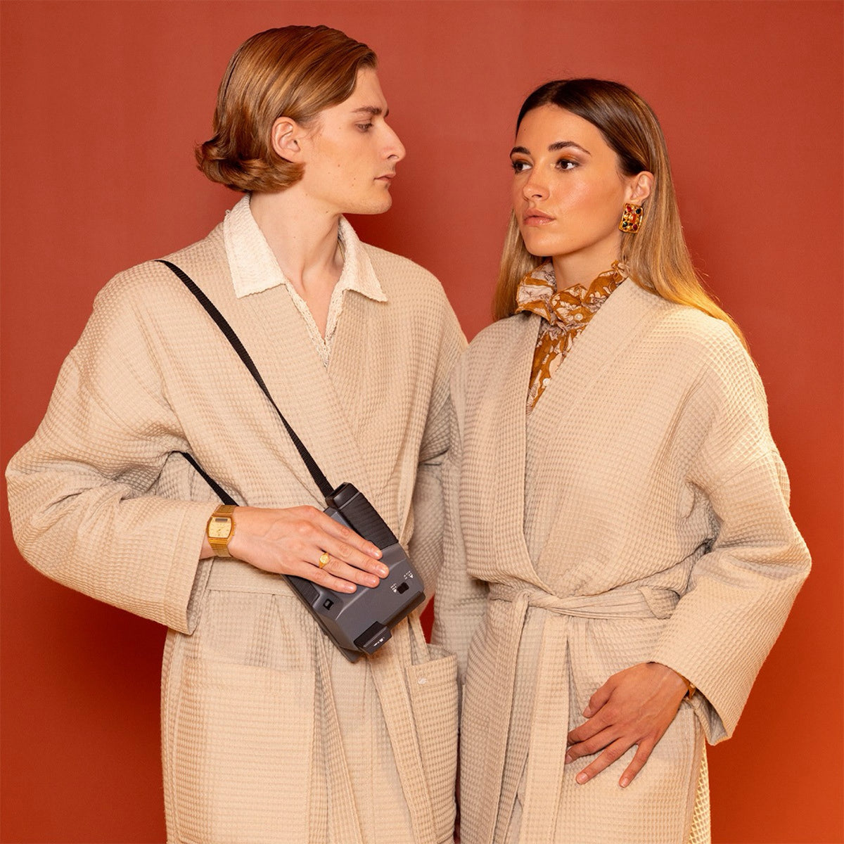 Two in Pierre Yves Delorme Astreena Bath Robes: one with a gold watch and camera, the other with patterned scarf and earrings