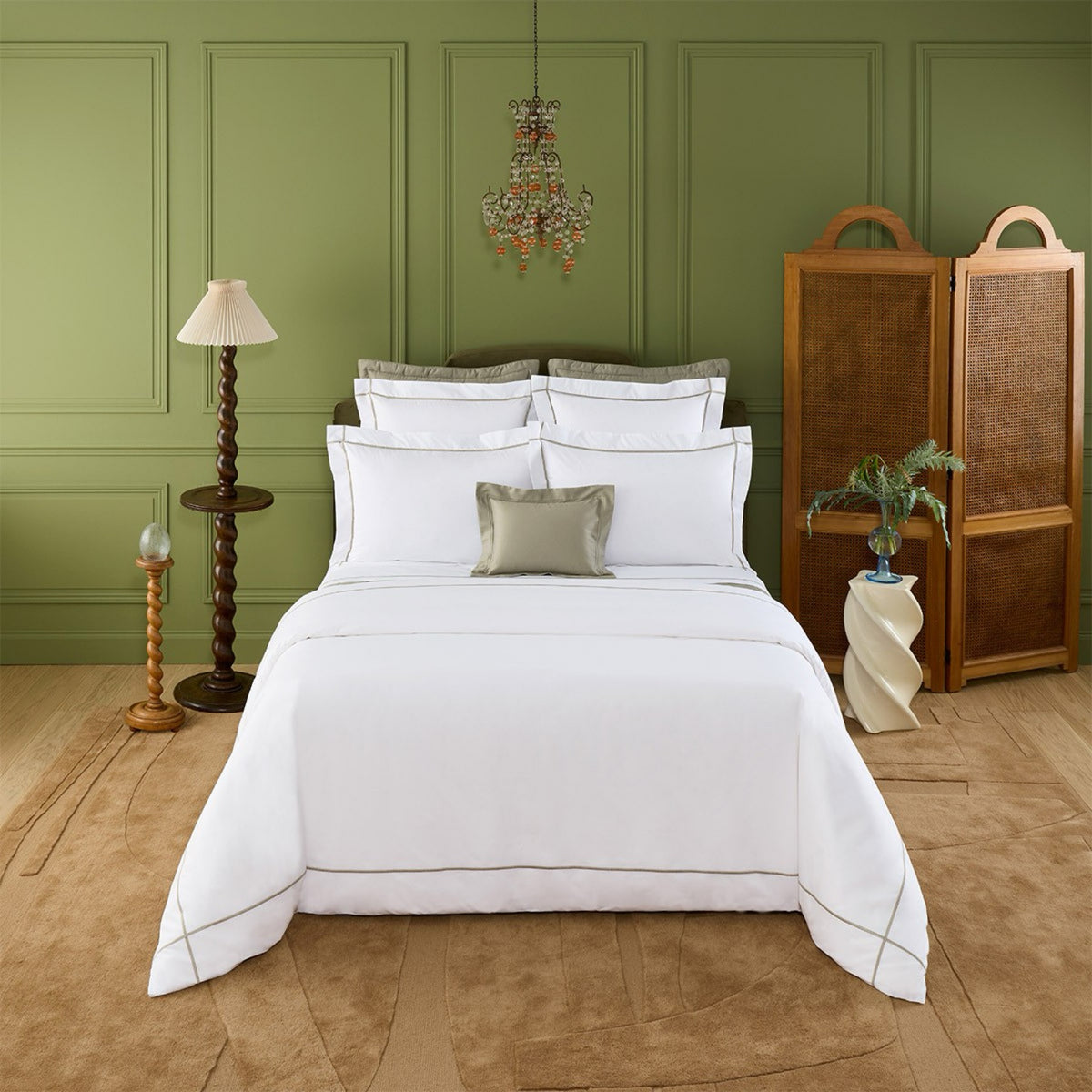 A neatly made bed with Kaki Yves Delorme Athena Bedding in a green-walled room, featuring lamps, a screen, and decor