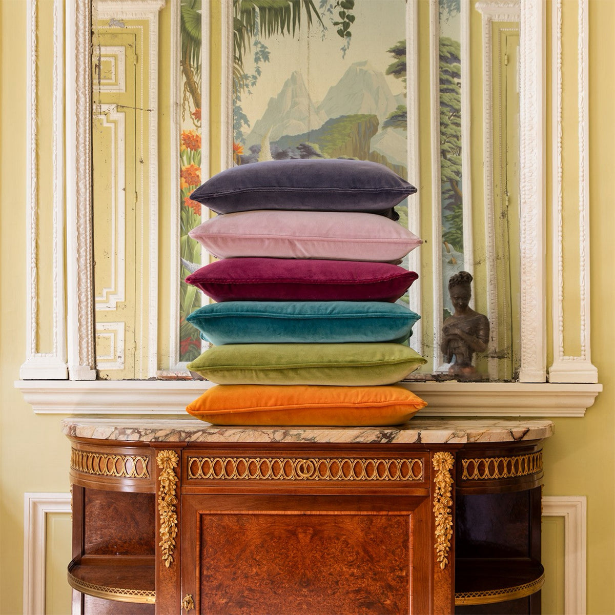A stack of six colorful Yves Delorme Divan decorative velvet pillows on a wooden console table.