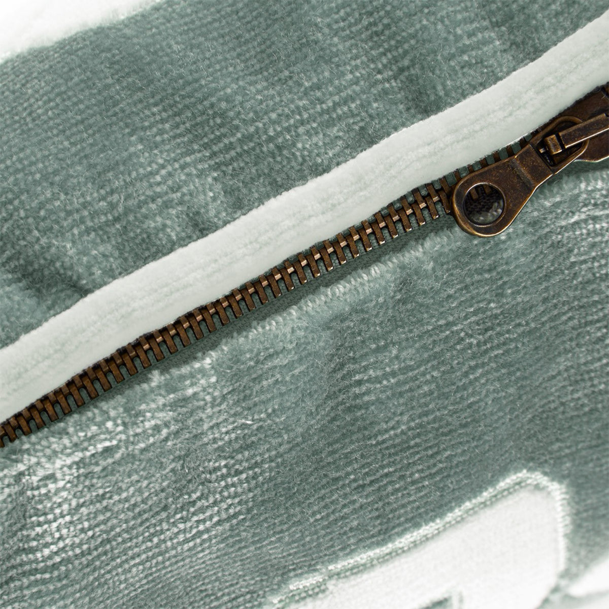 A close-up of a metal zipper on a sage green Genoa velvet cushion.