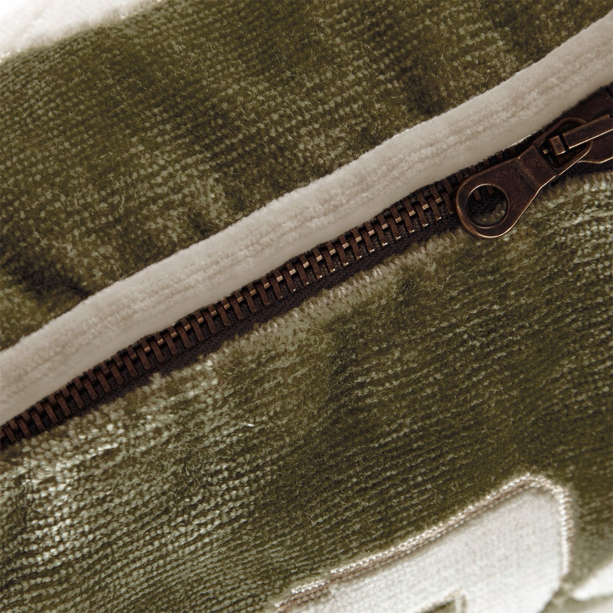 Close-up of a zipper on an olive green, interlaced pattern velvet decorative pillow.
