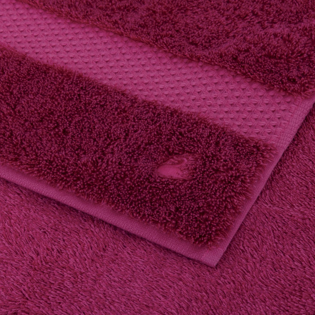 Three maroon Luxury Modal Towels with different textures and patterns are stacked on top of each other.