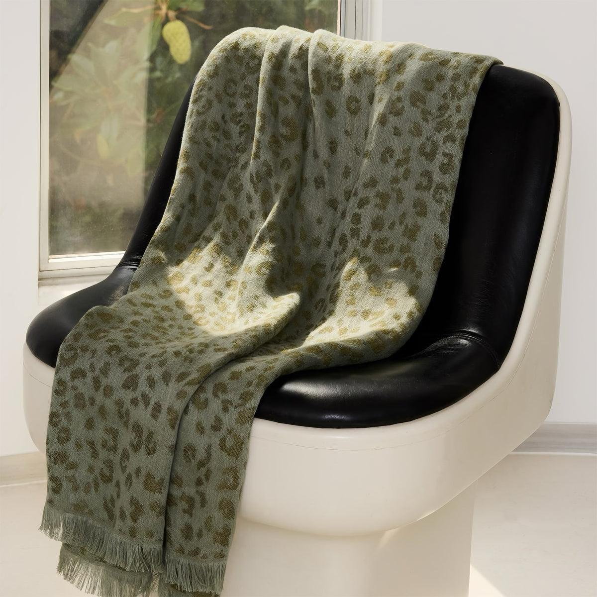 A Kaki Yves Delorme Fauve Throw draped over a modern black and white chair near a window.
