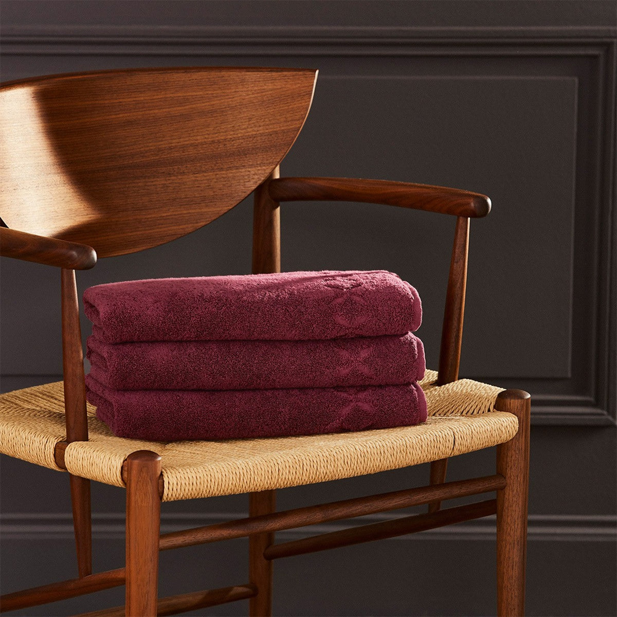 Folded Silo of Yves Delorme Nature Bath Towels on a Chair in Prune Color