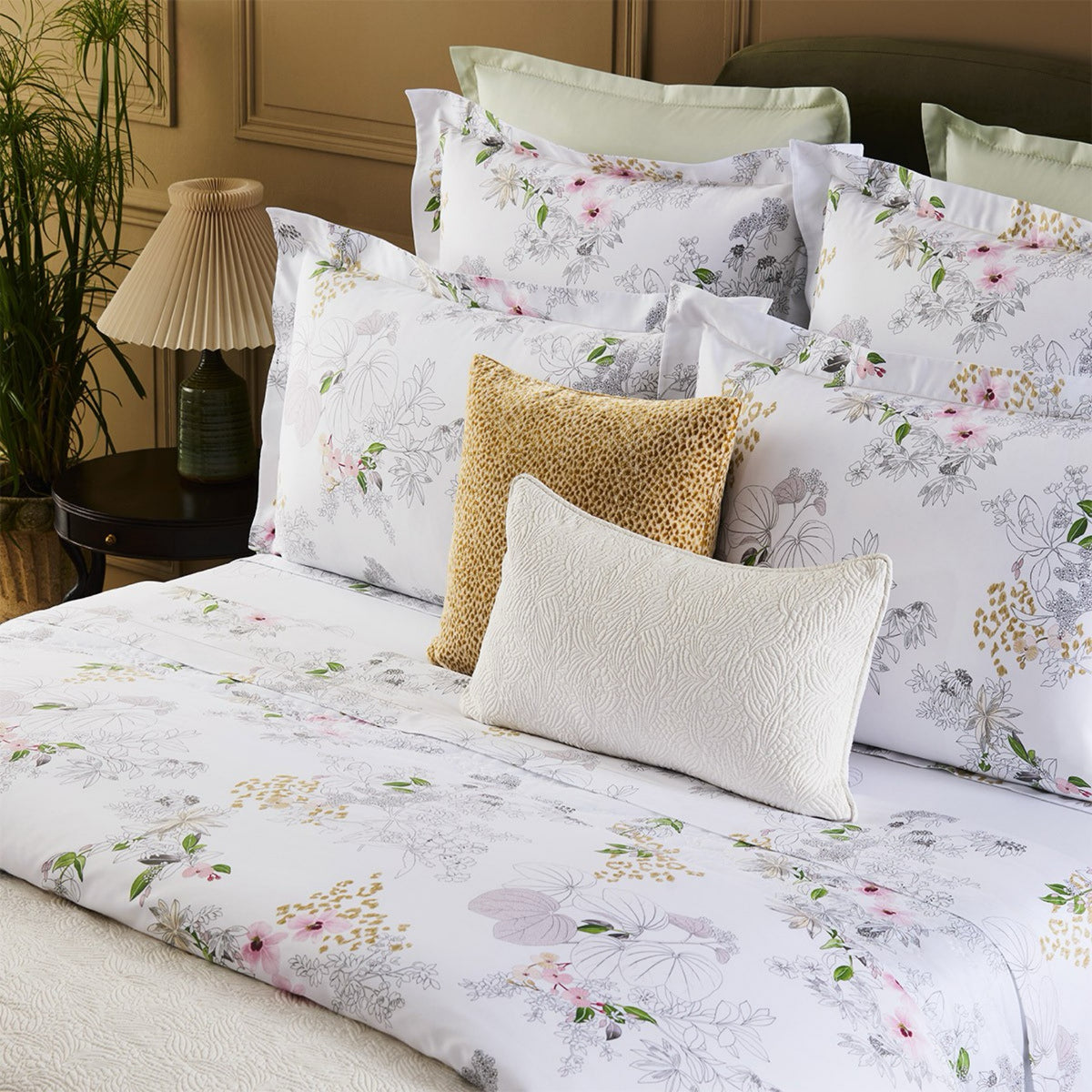 A neatly made bed with Yves Delorme Orchidée Collection floral duvet cover and cotton satin bedding in a softly lit bedroom