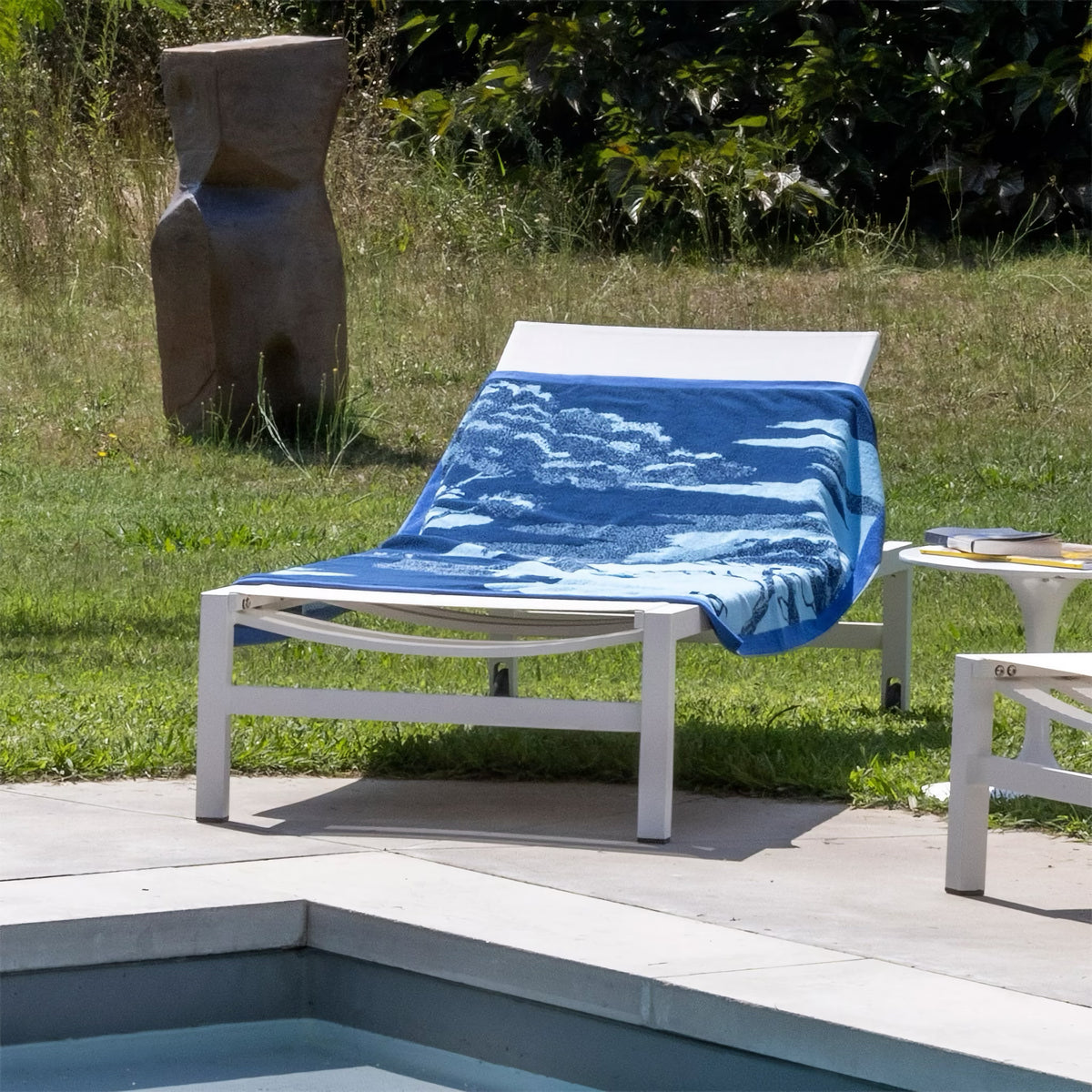 A lounge chair by the pool with an Yves Delorme Rive Beach Towel in Azure color
