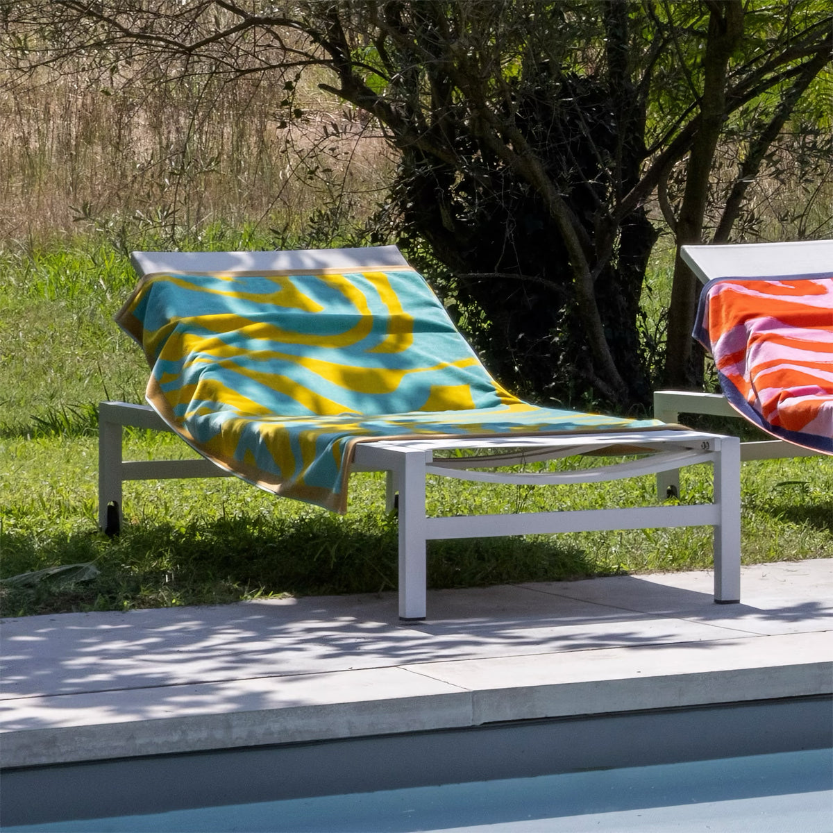 A white poolside lounge chair with a Lagon Yves Delorme Solaire Beach Towel