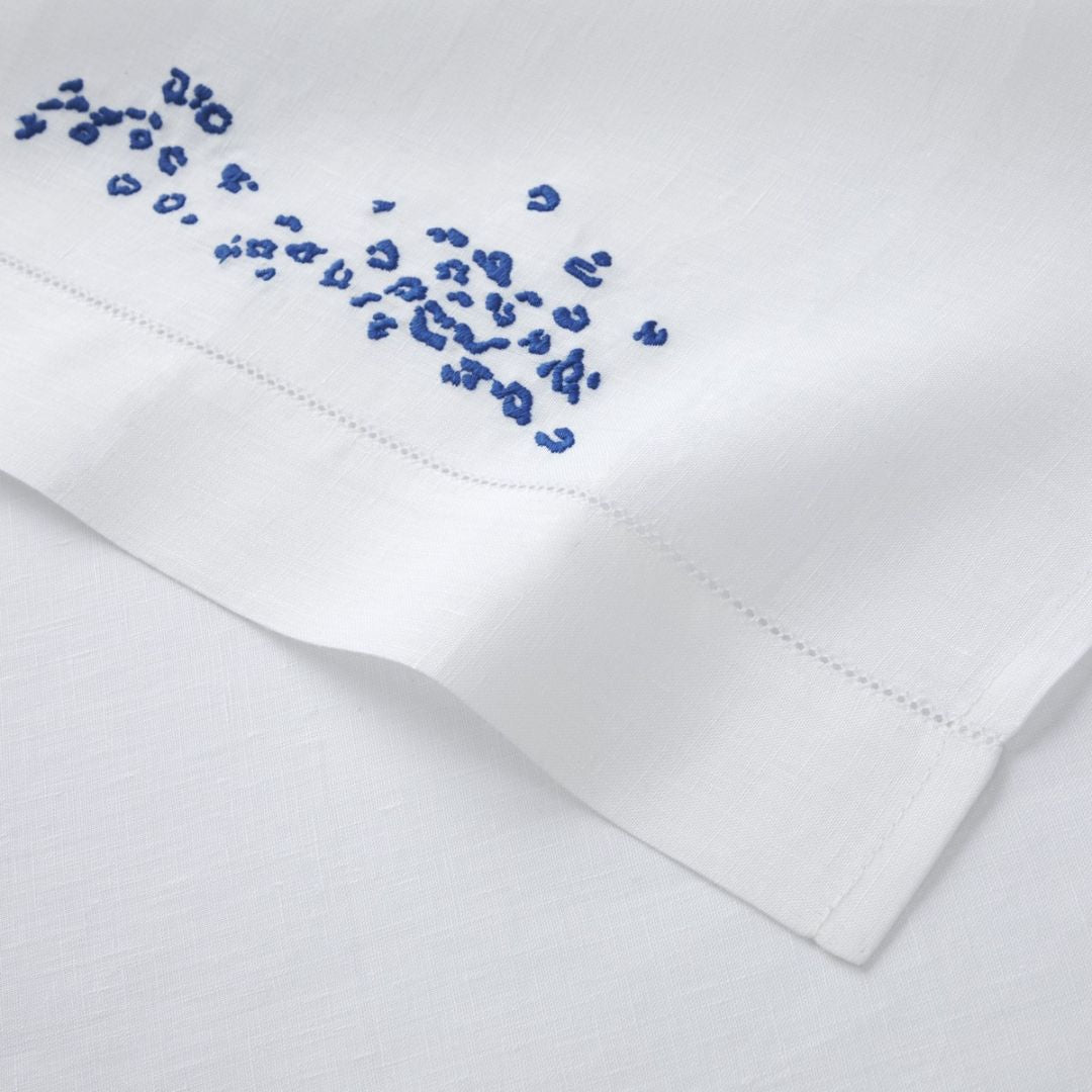 Close-up of a white linen guest towel set with a hemstitch border and small blue embroidered dots in one corner.