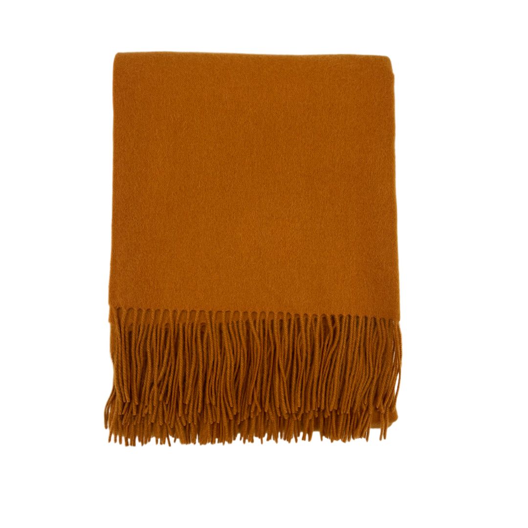 A folded burnt orange wool scarf with fringe, reminiscent of a woven blanket, displayed on a white background.