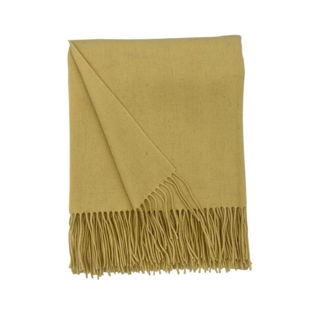 A folded mustard yellow merino cashmere throw with fringe detail, shown against a white background.