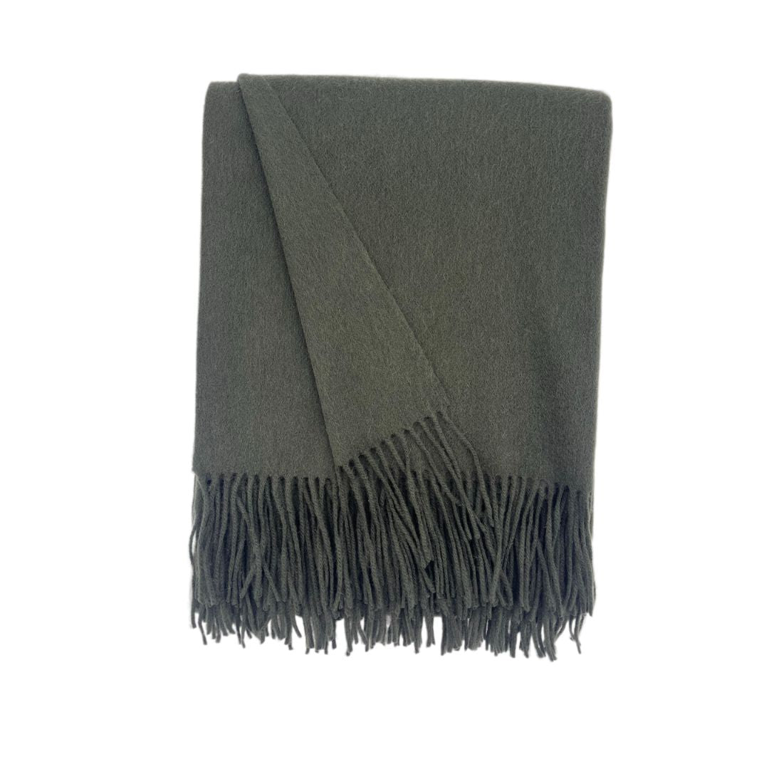 A folded dark green woven blanket with fringe, this solid colored merino cashmere throw is displayed on a white background.