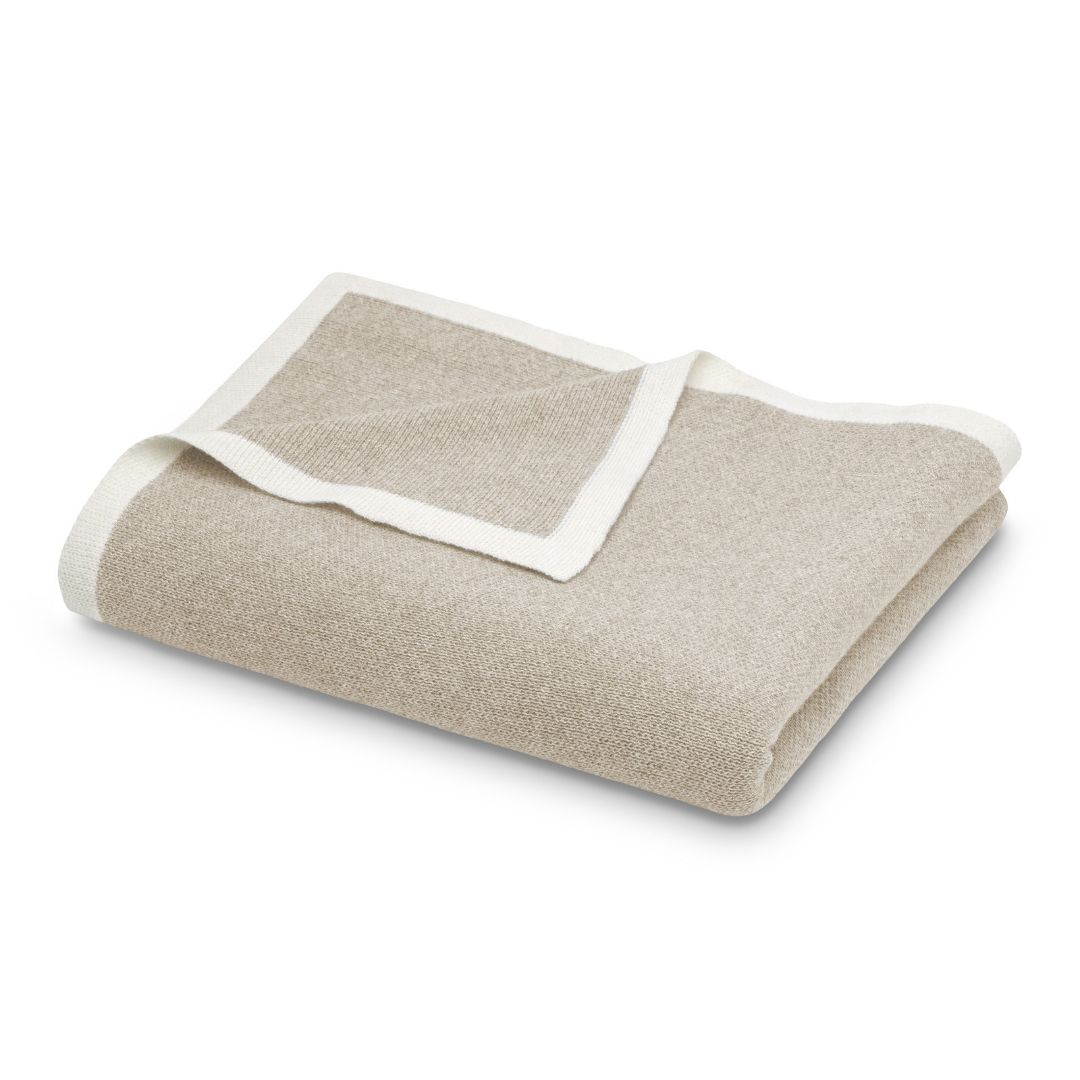 A folded tan Merino wool throw with a white border.