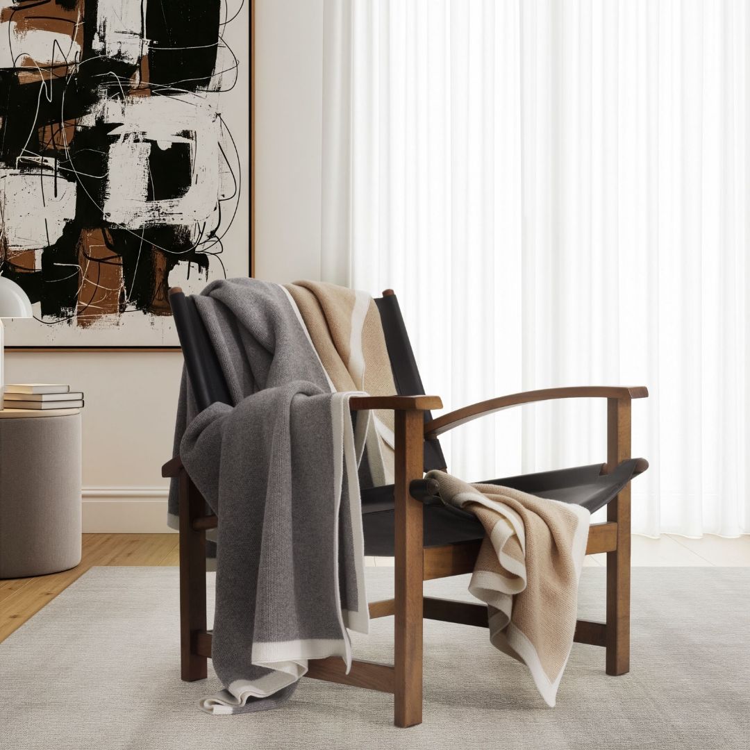A dark wood lounge chair draped with a luxurious cashmere silk throw and a gray Merino wool throw.