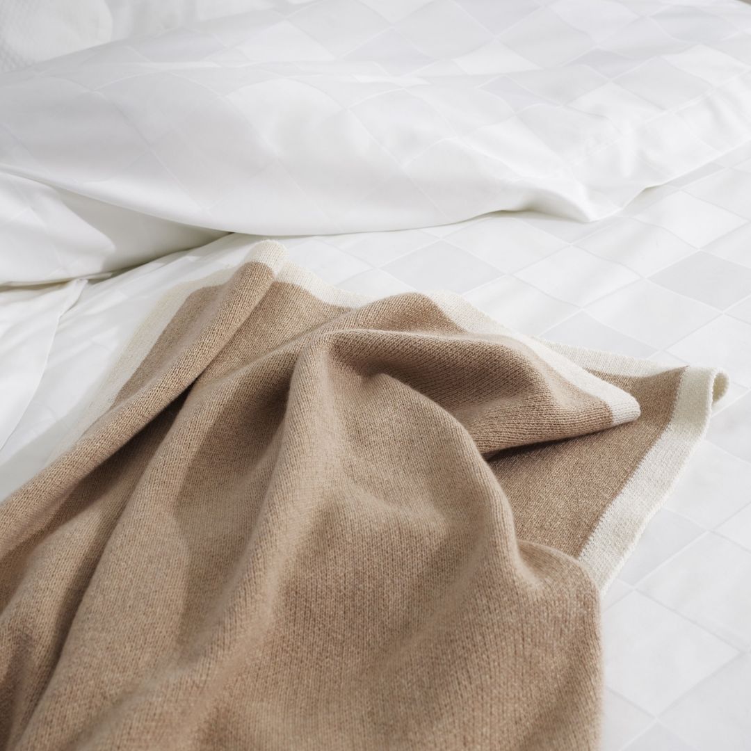 A luxury knit merino wool throw draped over a white checkered bedspread.
