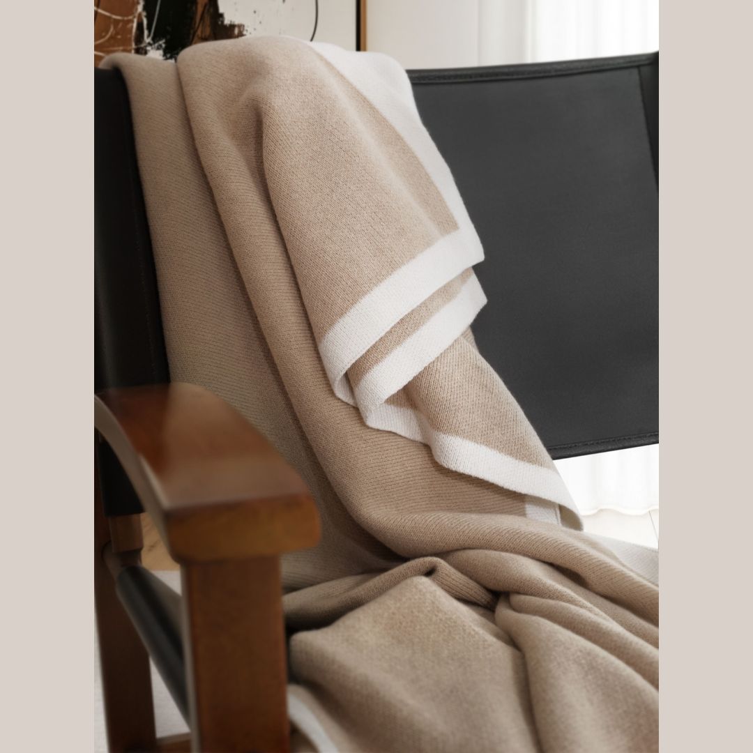 A tan merino wool throw with a white border draped over a black chair.