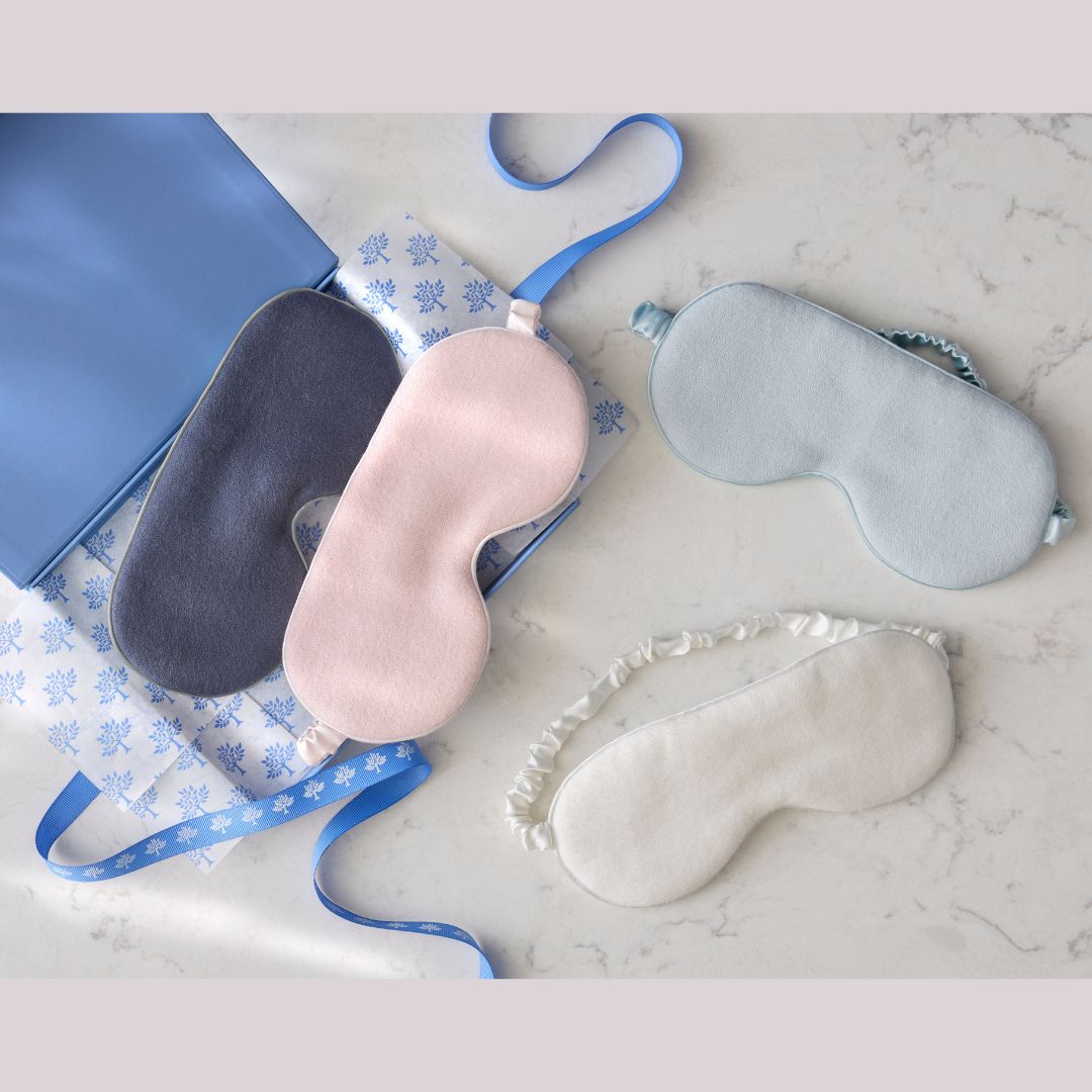 Four sleep masks in different colors on a marble surface with a blue case.