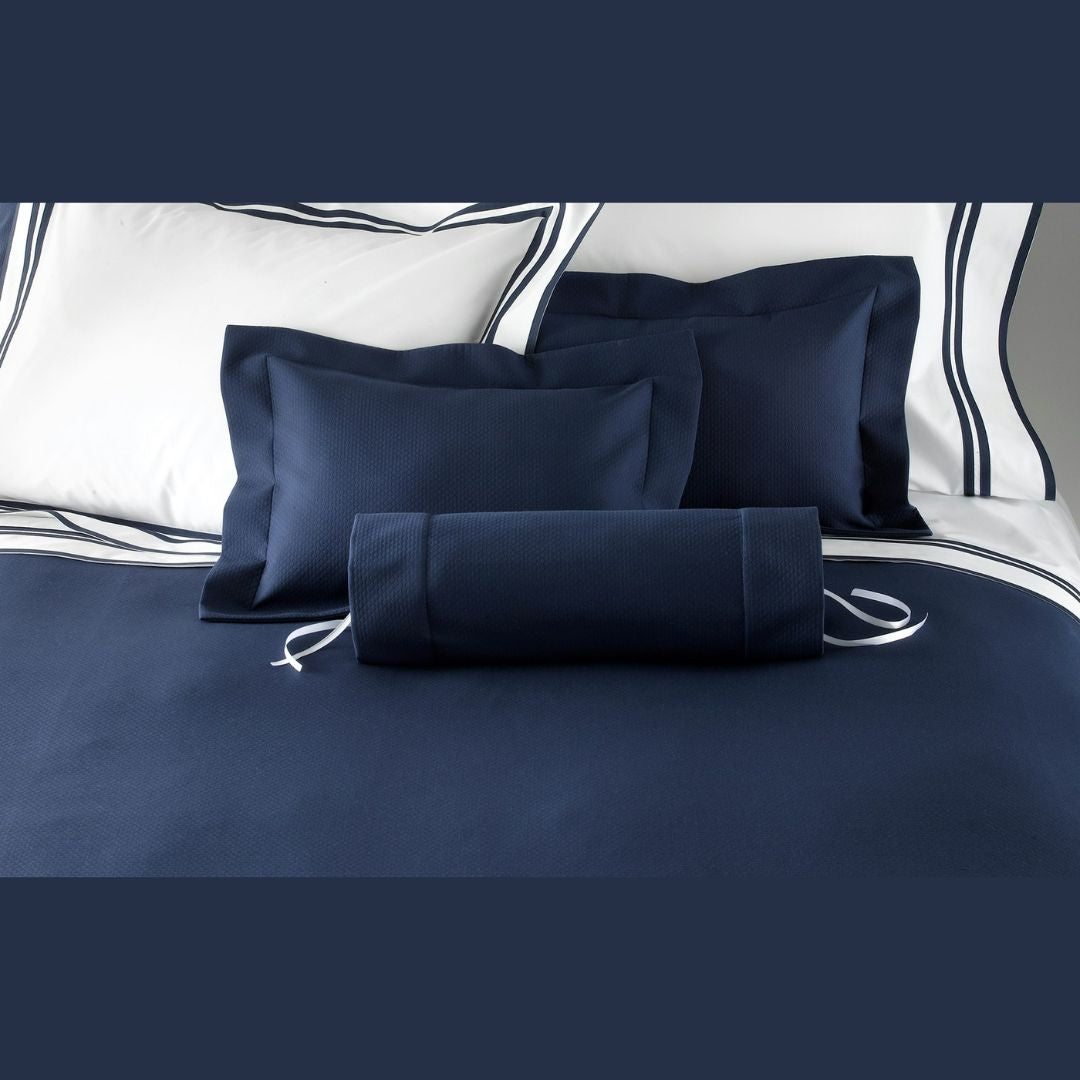 A neatly made bed with navy blue pillows, a navy blue bolster, and an Elliot Coverlet—an essential modern bedroom staple.