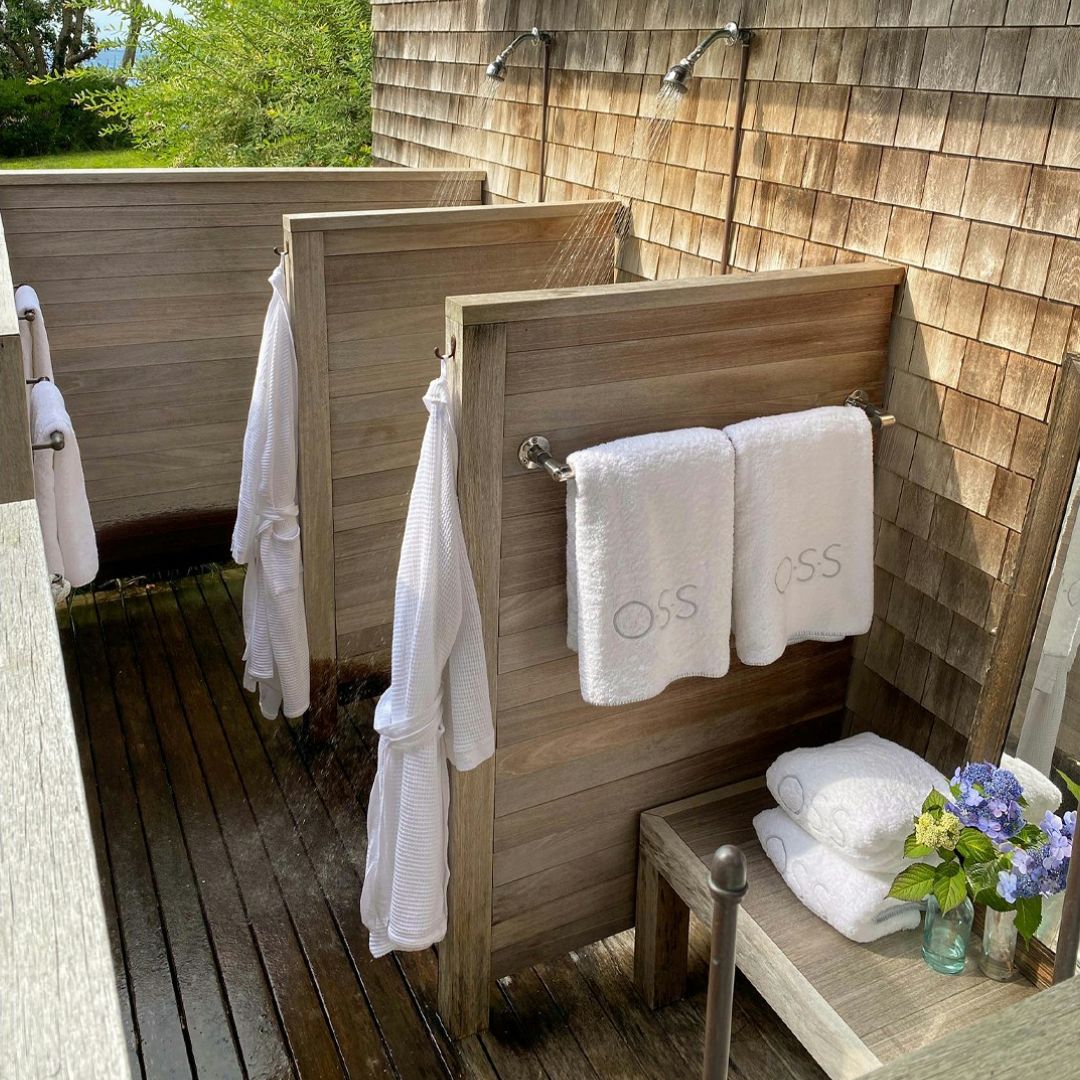 Outdoor shower area with wooden walls, white towels, and a small table with flowers.