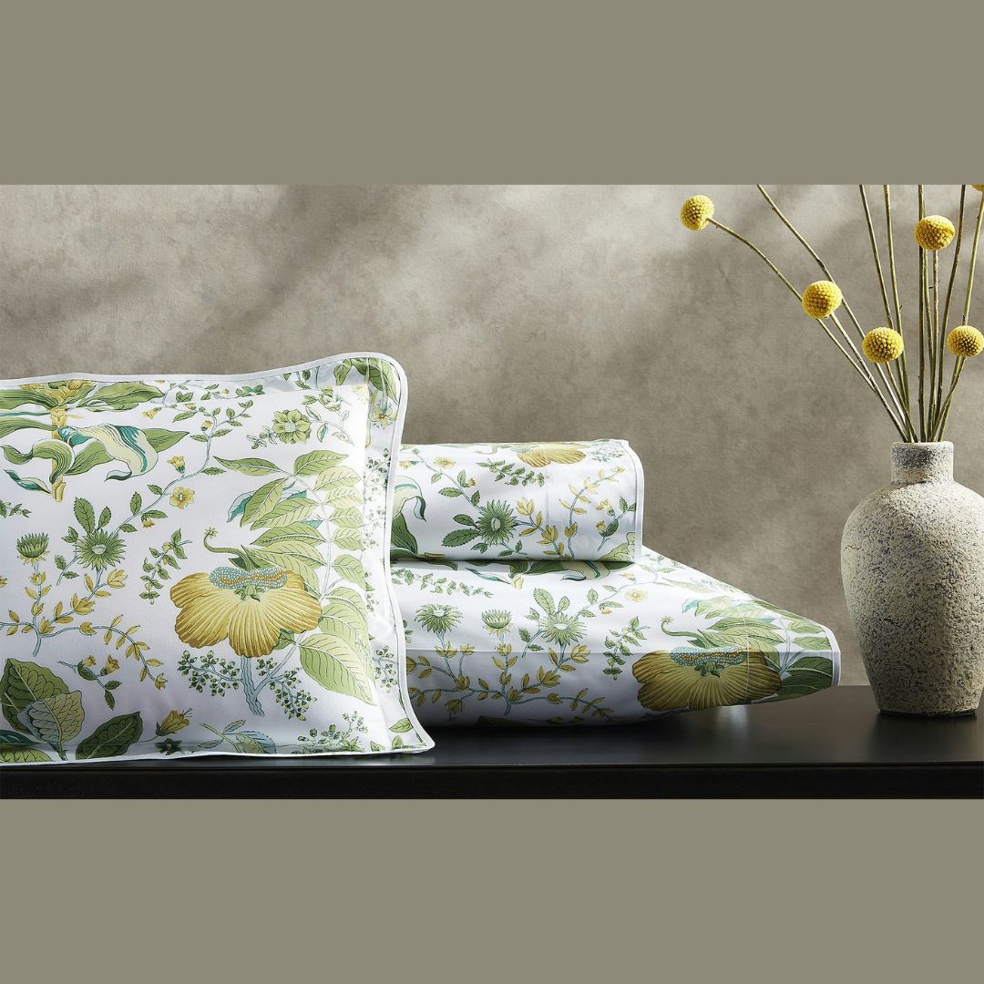 Floral-patterned shams and pillowcases on a surface with a vase of yellow flowers in the background.