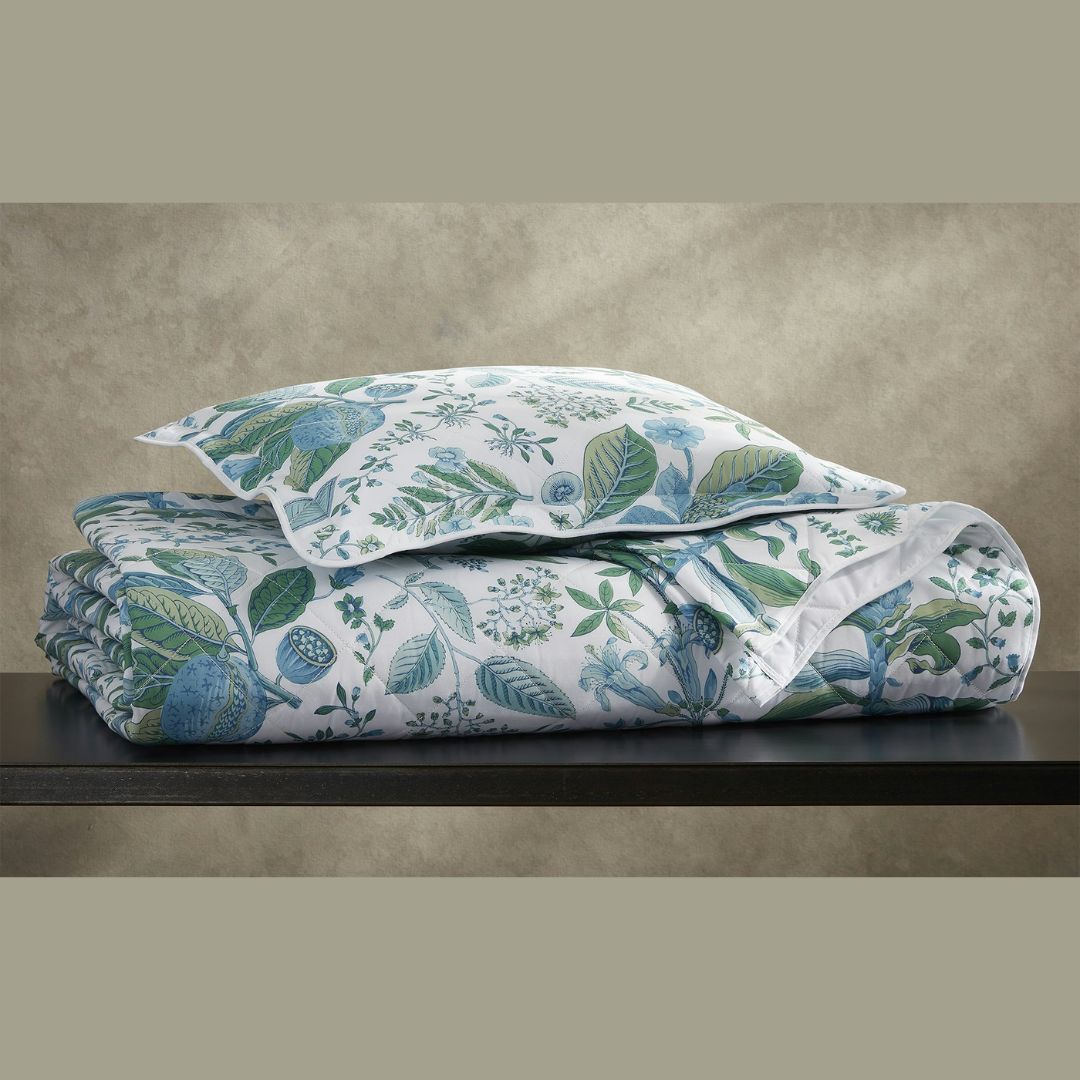 A folded comforter and pillow in Egyptian cotton percale with a green and blue leaf pattern sit on a dark table.