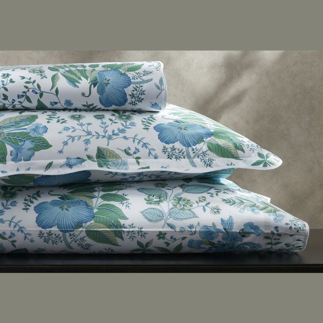 Three stacked pillows with white Egyptian cotton percale covers in a blue and green floral pattern against a neutral background.