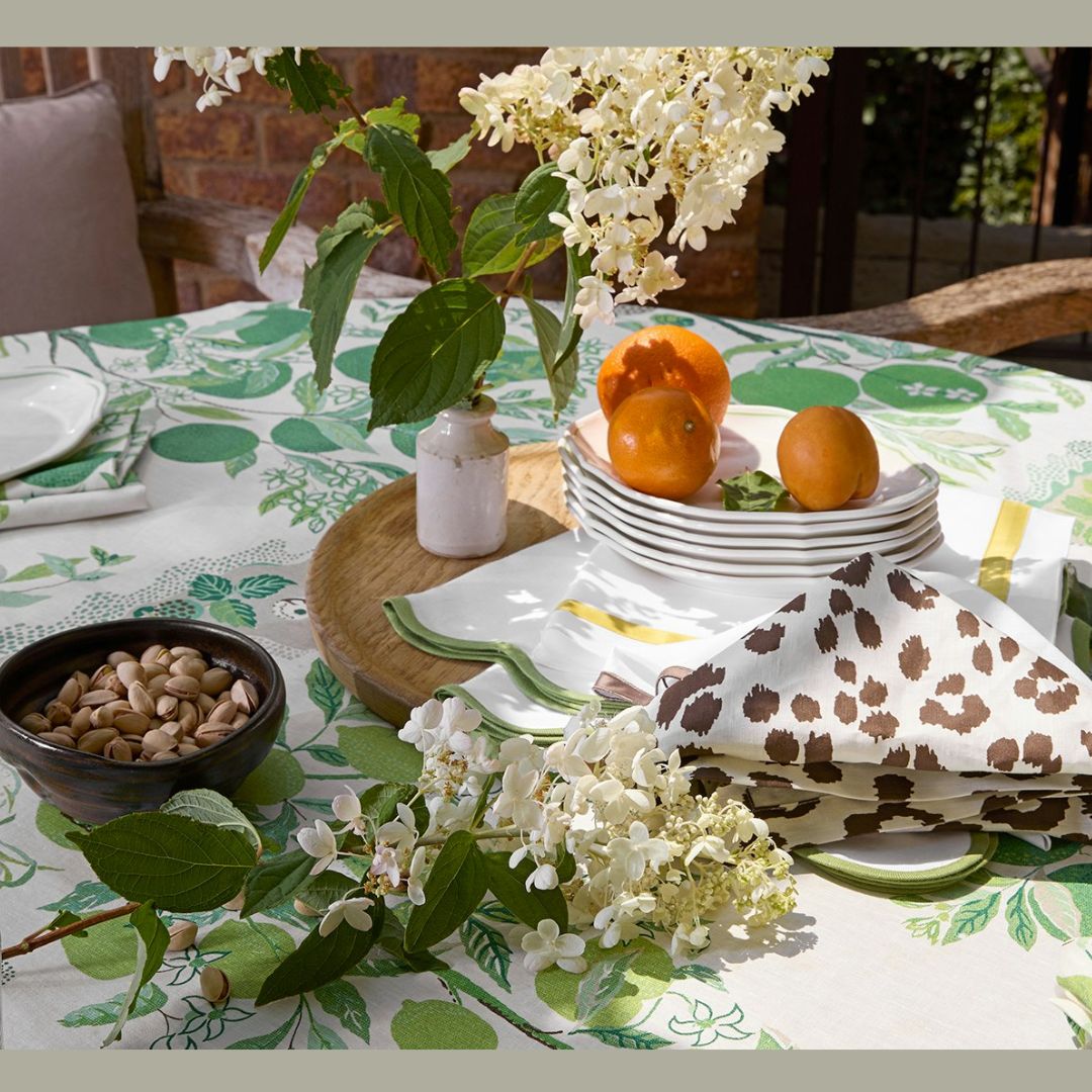 Table set with plates, apricots, pistachios, floral tablecloth, Matouk table linens, and a folded napkin.