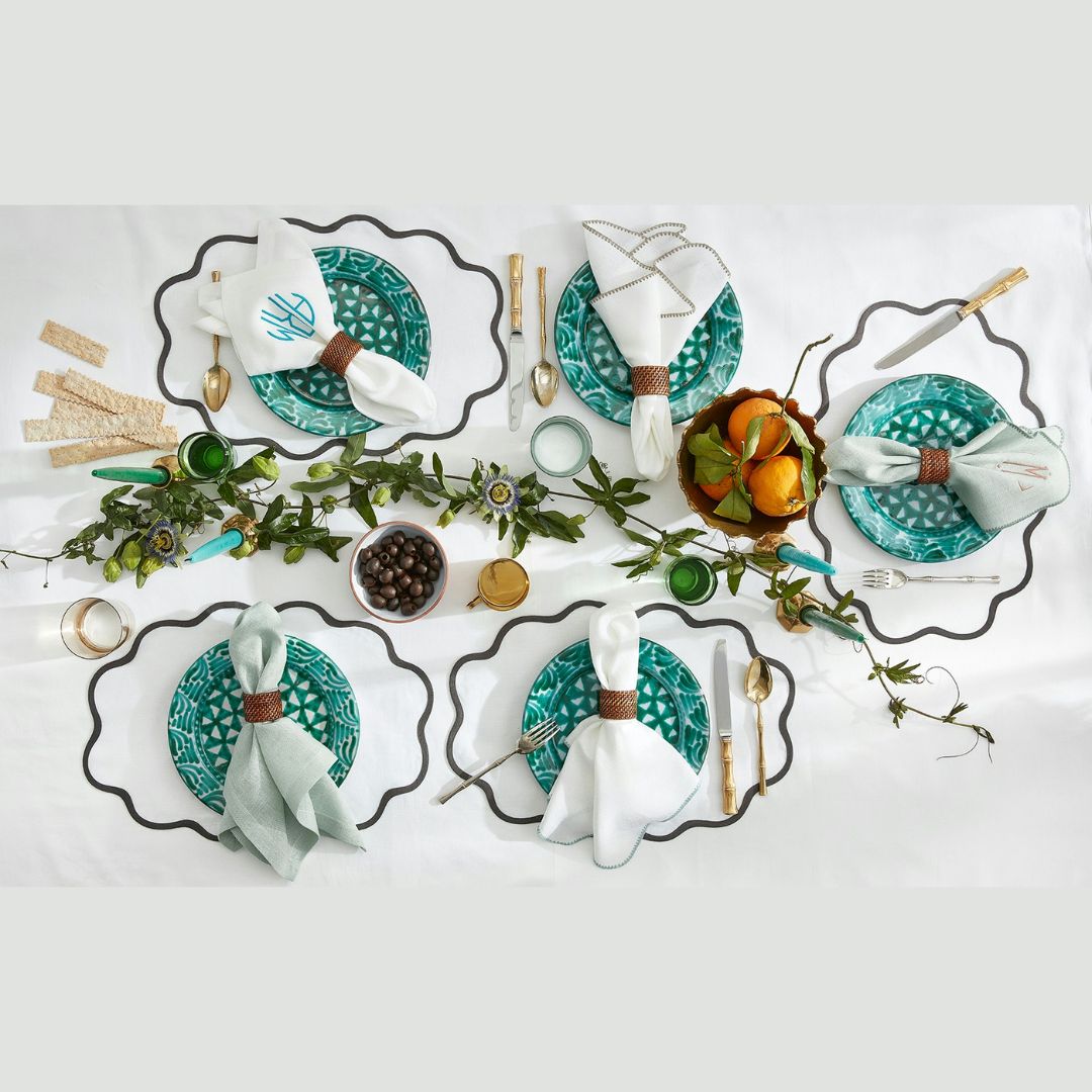 Table set for four with turquoise plates, Matouk table linens, silverware, greenery, and a bowl of oranges as a centerpiece.
