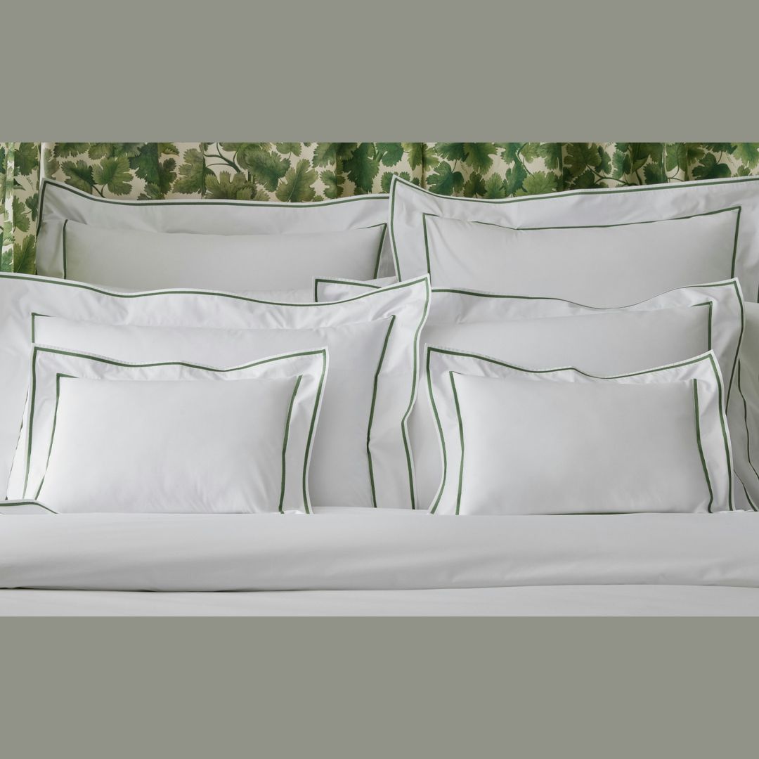 A neatly made bed with Matouk Ansonia luxury percale sheets, white pillows, and green leafy wallpaper.