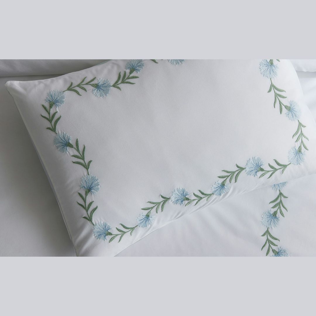 A white pillowcase with light blue embroidery, part of our embroidered floral bedding in Ceylon percale.