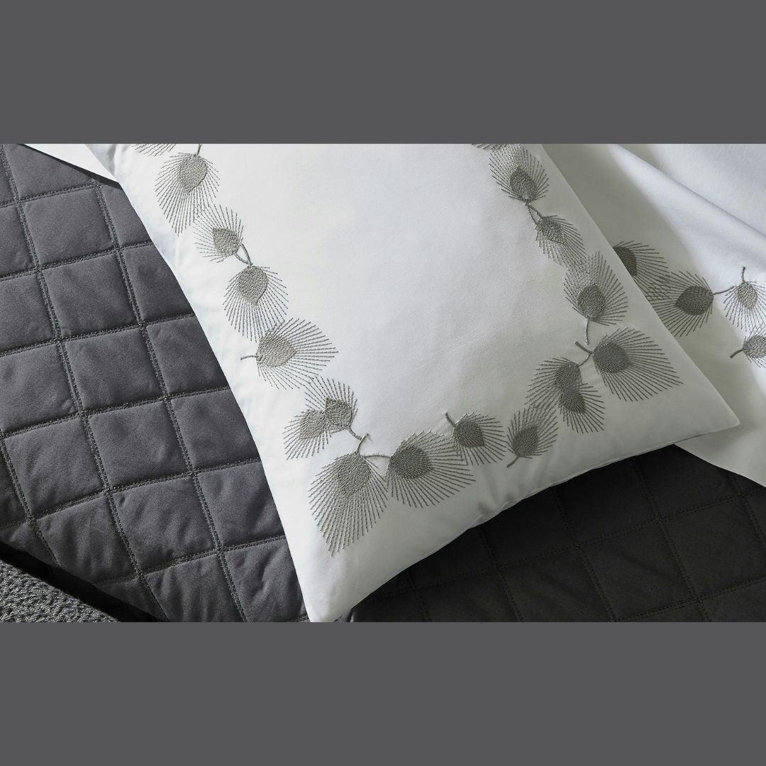 White pillowcase with gray leaf embroidery on a dark gray quilted bedspread; luxury bedding at its finest.