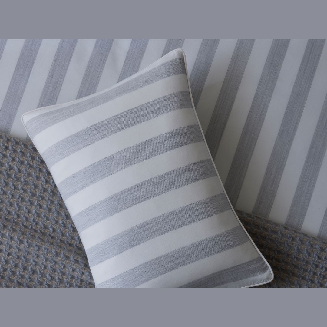 A white and gray striped pillow rests on Matouk Lana Bedding with a textured gray blanket nearby.