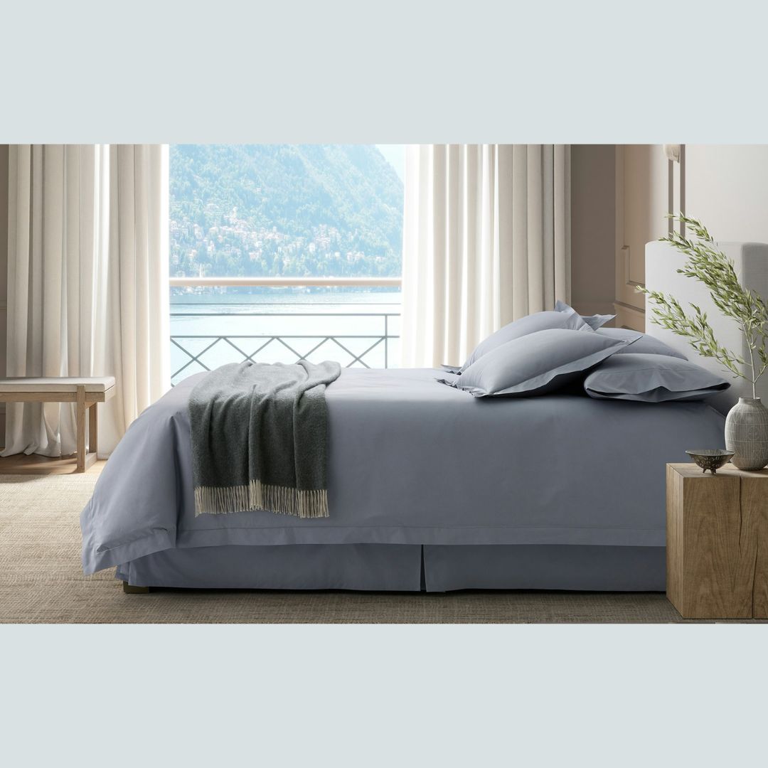 A neatly made bed with Percale bedding faces a window with lake views, light curtains, and natural light streaming in.