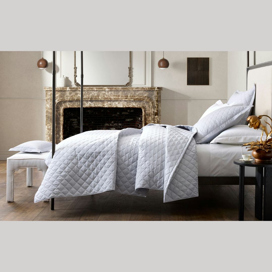 A neatly made bed with a Milano percale quilt sits in front of a fireplace in this modern bedroom.