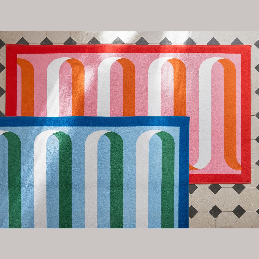 maotuk ribbon beach towels in ocean and flamingo laying on a marble tiled floor