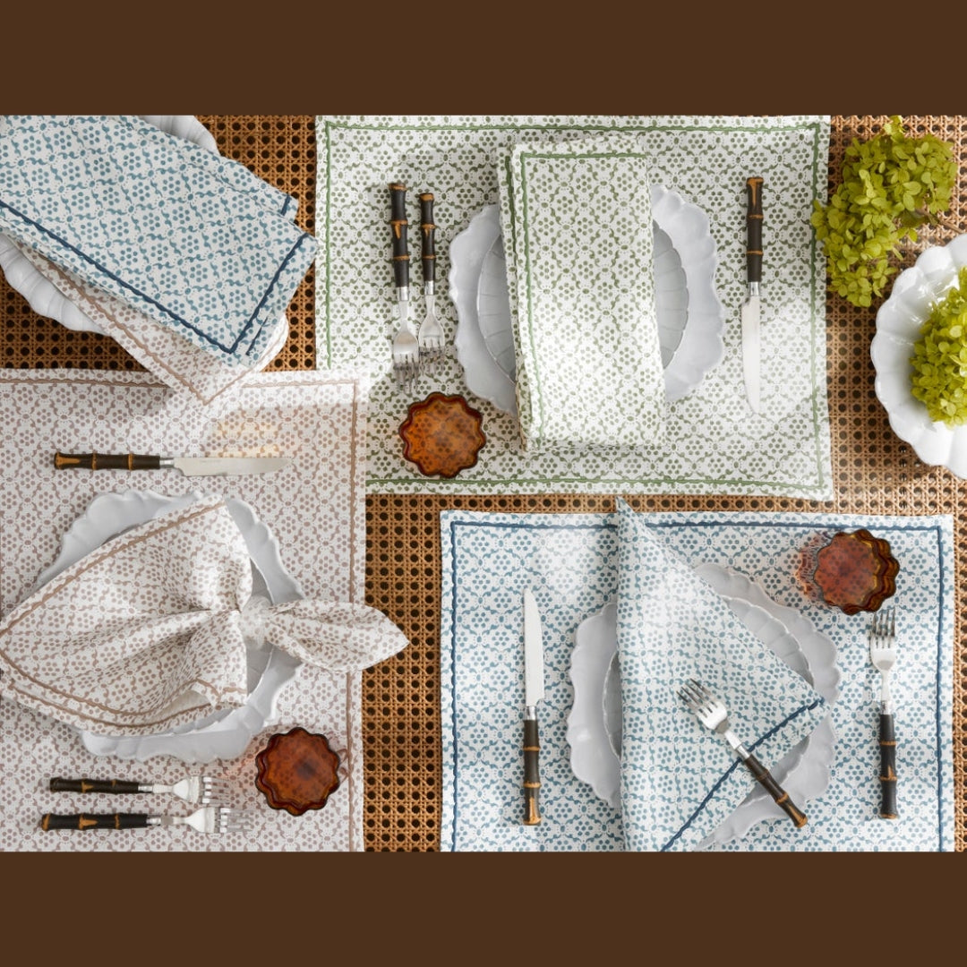 Three place settings with block print napkins, plates, cutlery, and small amber glass dishes on a woven placemat.