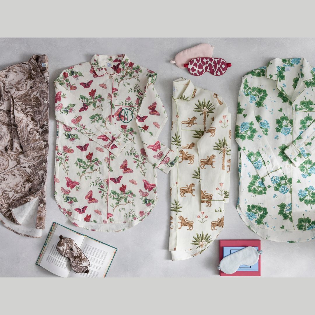 Four patterned luxury sleep shirts, two sleep masks, and two open books arranged on a light gray surface.