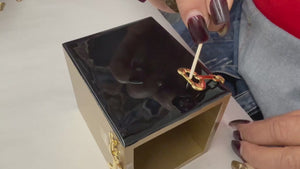 Video of the Mike and Ally Hampton brush box being made. An artist is laying the embellishment, a gold stirrup, into black enamel.