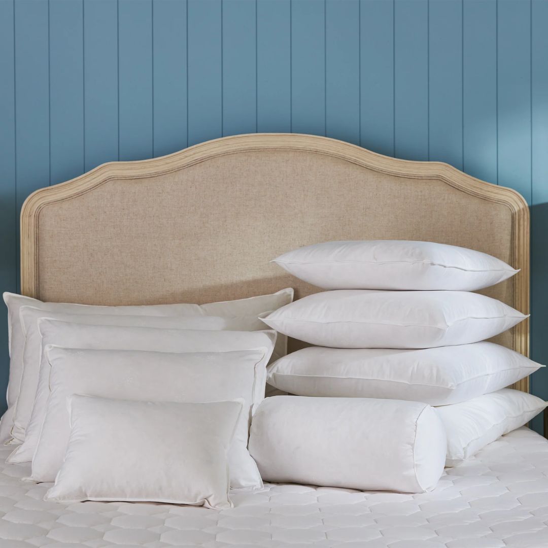 A bed with a beige fabric headboard and decorator insert pillows in front of a blue paneled wall.